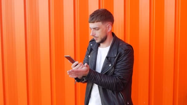 Młody człowiek z brodą puka jego rękę na telefon, telefon nie łapie sieć, słabej komunikacji mobilnej. pomarańczowo, zwolnionym tempie — Wideo stockowe