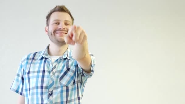 Αξύριστος Καυκάσιος νεαρός σε ένα πουκάμισο είναι μόνιμη και δείχνει ένα δάχτυλο για τη φωτογραφική μηχανή, μια ιδέα, γκρο πλαν, λευκό φόντο — Αρχείο Βίντεο