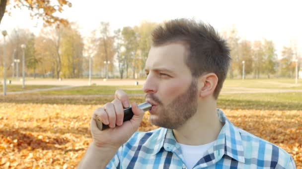 Mladý pohledný muž s bradkou, ineptly vape v ulicích a kašle, close-up, zpomalené — Stock video