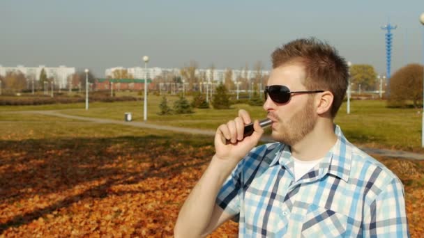 Cooler kaukasischer Typ in schwarzer Brille und Hemd raucht Dampf, draußen, Zeitlupe, Vaporizer — Stockvideo