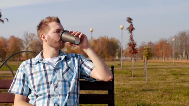 ひげを持つスタイリッシュでハンサムな若い白人男がベンチに座ってと飲むコーヒー、クローズ アップ、スローモーション、コピー スペース、屋外 — ストック動画