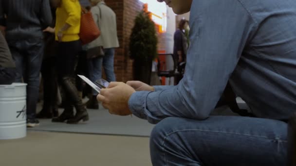 Ein Männchen sitzt in der Warteschlange, bedient sich des Smartphones und löst seine Angelegenheiten — Stockvideo
