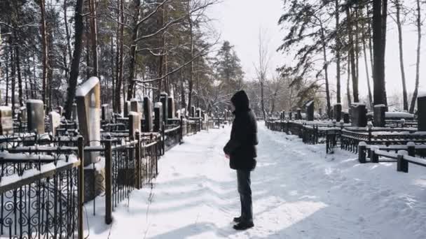 Людина оплакує або сумує за померлим на цвинтарі або кладовищі взимку в лісі — стокове відео
