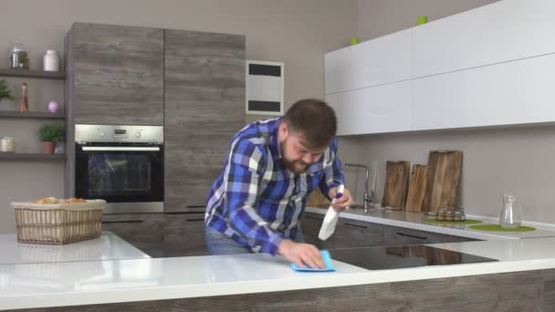 Grueso hombre caucásico alegre con una barba haciendo la limpieza en la cocina, lavando la encimera, interior moderno, cámara lenta, limpieza de la casa — Vídeo de stock