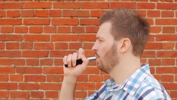 Guapo elegante hombre fumando vap contra una pared de ladrillo y mirando a la cámara, lento-mo, de moda — Vídeos de Stock