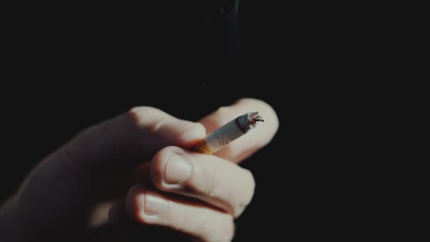 Pojęcie szkodliwości palenia, zbliżenie na palec otrzepuje popiołu z papierosa na tle ciemności — Wideo stockowe