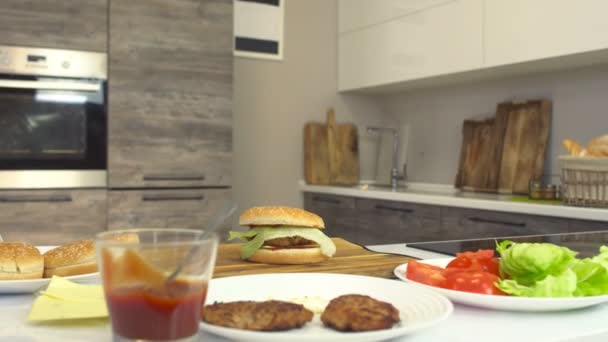 Hamburguesa de queso fresca y jugosa cocinada en una cocina moderna y productos, ingredientes para una hamburguesa y hamburguesa con queso, fondo — Vídeos de Stock