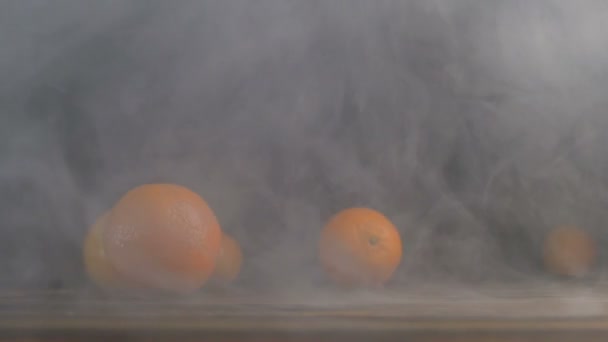 Мандаринские апельсины или мандарины катятся по столу в дыму в замедленной съемке — стоковое видео