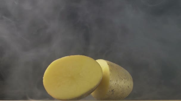 Två halvor av en skära rödbrun potatis är på bordet i röken i slow motion — Stockvideo