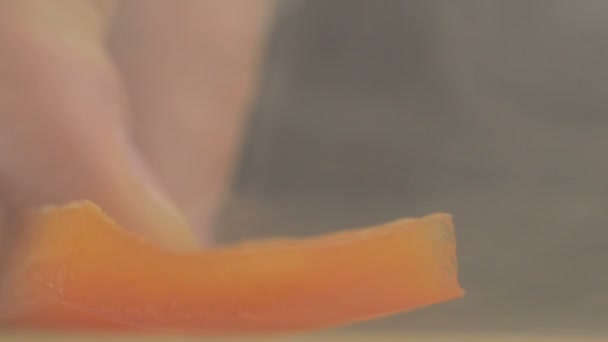 Knife cuts off a piece of red sweet bell pepper or capsicum in smoke and slowmo, macro — Stock Video