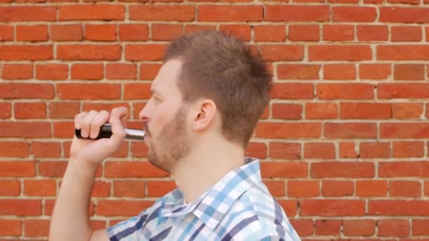 Pohledný stylový muž kouří vape proti cihlové zdi a hledí do kamery a ponechává rám, close-up, slow-mo, životní styl — Stock video