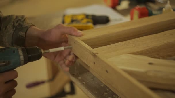 Carpenter or Joiner drills a hole in a wooden structure with screw gun or power drill in the furniture workshop — Stock Video