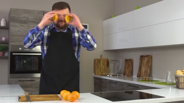 A brutal man with a beard is indulging and fooling around with oranges at home in the kitchen, slow motion, fool around — Stock Video