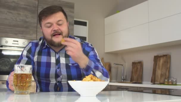 Hombre con barba bebiendo cerveza en la cocina y tocando papas fritas, primer plano, adiposidad, cámara lenta, hormona femenina — Vídeo de stock