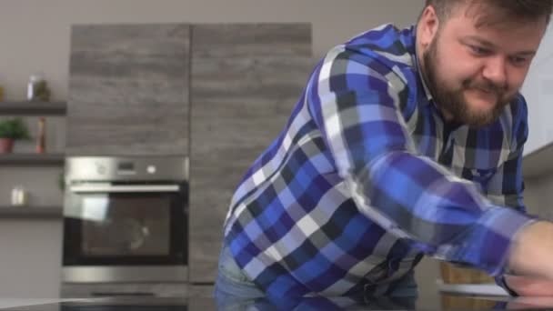 ヒゲ面のデブ男自宅でスローモーション モダンなキッチンのテーブルを洗う — ストック動画
