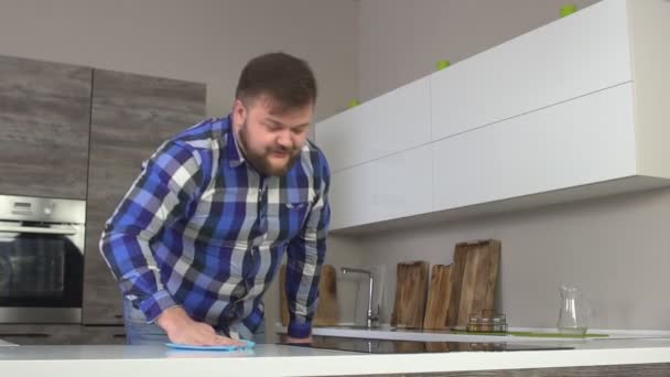 Glada hemmagjord mannen i en rutig skjorta tvättar ett bord i kök, modern interiör, långsamma-mo, hushållsarbete — Stockvideo