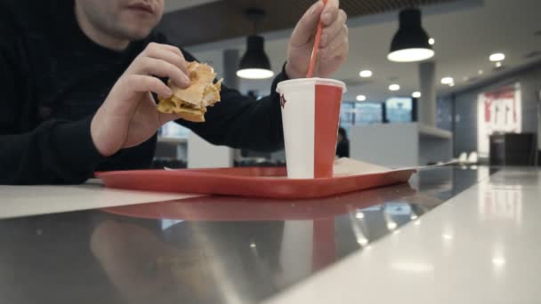 Macho come hambúrguer ou chiken hambúrguer, bebe água espumante no restaurante fast food — Vídeo de Stock