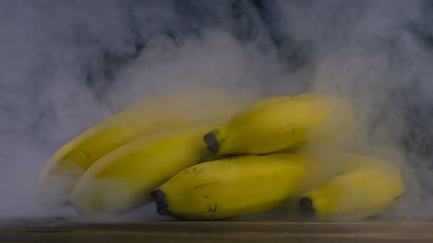 Manojo de plátanos Cavendish están sobre la mesa, el humo sopla por detrás en slow mo, de cerca — Vídeo de stock