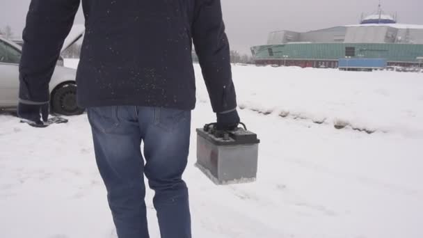 Mężczyzna niesie i instaluje akumulatora samochodowego w samochodzie, zima. śnieg, zwolnionym tempie — Wideo stockowe