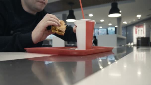 Chico come humburger o chiken burger, bebe agua carbonatada dulce en restaurante — Vídeos de Stock