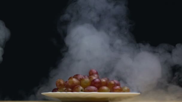 En tallrik druvor spinning i rök i slow motion på svart bakgrund — Stockvideo