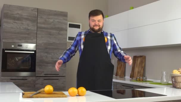 Жестокий человек в фартуке дурачится на современной кухне с апельсинами, замедленной съемкой, вегетарианцем — стоковое видео
