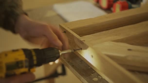 Ács vagy Asztalos rögzít egy fából készült termék, csavar és csavaros fegyvert vagy erő fúró a bútorok műhely — Stock videók