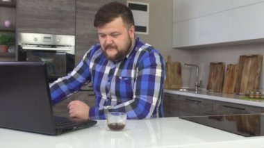 Modern ev mutfak, hayal kırıklığı, öfke, ağır çekim bir dizüstü bilgisayar üzerinde çalışan bir sakallı kızgın adam