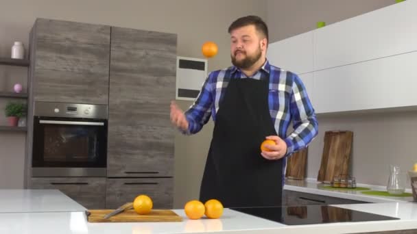Человек с бородой и фартуком бросает апельсин на современной кухне, здоровую диету, замедленное движение — стоковое видео