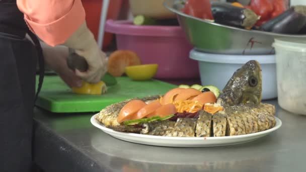Um cozinheiro na cozinha corta um limão para decorar um prato de peixe carpa, close-up, restaurante, câmera lenta — Vídeo de Stock