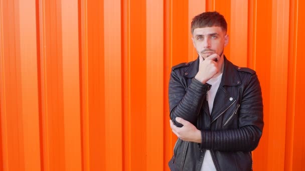 Ein junger Modetyp mit Bart und nachdenklichem Gesicht steht und denkt, orangefarbener Hintergrund, Kopierraum, Zeitlupe — Stockvideo