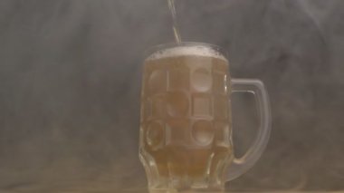 Bira cam içinde taze bira dökülür bir sis, yakın çekim, siyah arka plan, ağır çekim bükülmüş