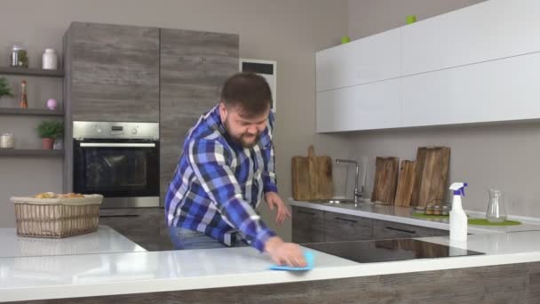 Homem caseiro alegre em uma camisa xadrez lava uma mesa na cozinha, interior moderno, slow-mo, interior — Vídeo de Stock