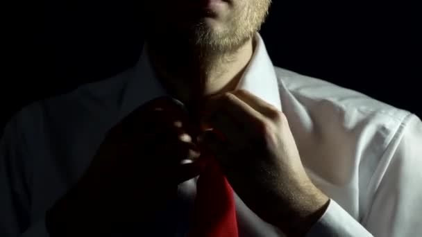 Un hombre con barba y camisa blanca se ata la corbata y se abotonan la camisa, primer plano, fondo negro, hombre de negocios — Vídeo de stock