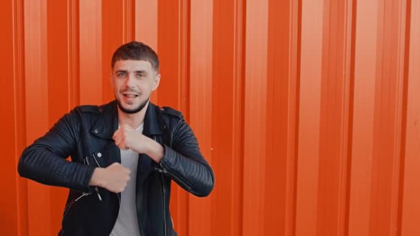 Vrolijke happy man in een zwart lederen jas beweegt dansen en zingt tegen de oranje achtergrond — Stockvideo