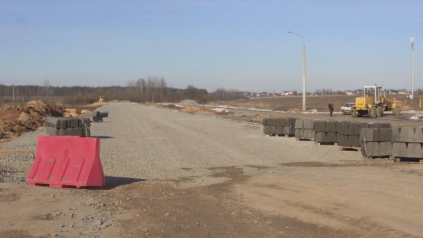 Un hombre es un trabajador en un chaleco de señal para colocar un bloque contra el paso donde se está construyendo una nueva carretera, la seguridad — Vídeos de Stock