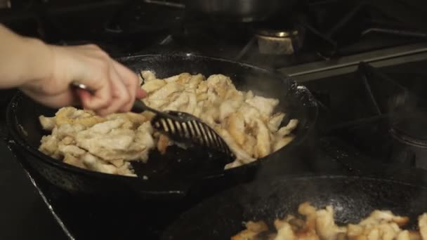 Cozinheiro mistura pedaços de carne de frango assada em uma frigideira ou frigideira na cozinha do restaurante no fogão a gás em câmera lenta — Vídeo de Stock