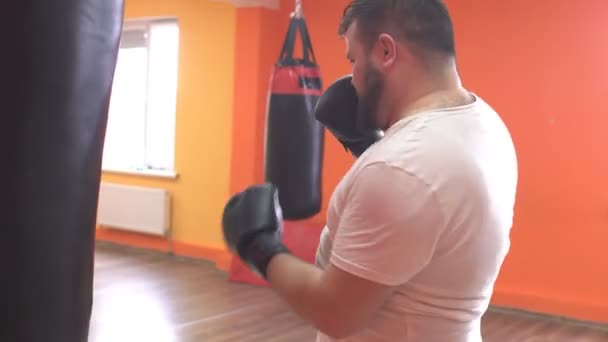 Kövér, szakállas ember fáradt-ból képzés boksz a lyukasztó zsák a tornateremben, sport — Stock videók