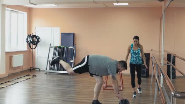 Fat man training with woman instructor and doing exercises in fitness center. Thick obese guy together with personal slim coach do physical jerks in gym. Overweight male and female trainer with — Stock Video
