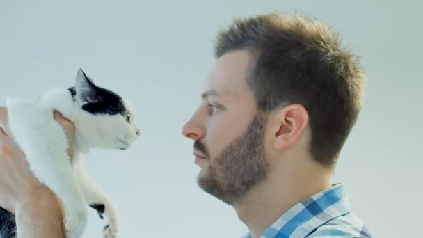 Ernster bärtiger Mann hält schwarze und weiße Hauskatze in den Händen und schaut sie an — Stockvideo