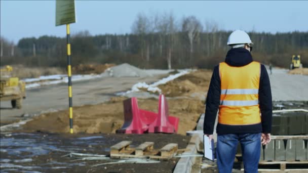 Inspector surveyor is watching the process of road construction before laying of roadbed or pavement material by heavy building equipment — Stock Video