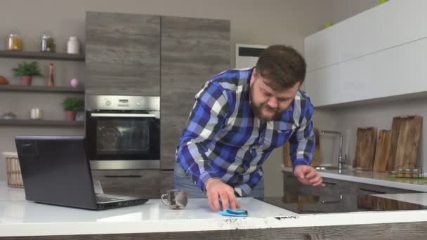 Seorang pria Kaukasia membersihkan dan mencuci kopi tumpah di dapur, laptop, gerakan lambat — Stok Video