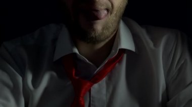 Sakallı ve Beyaz gömlekli bir adam dudaklarını yalıyor ve ipuçları seks, yakın çekim, siyah arka plan, erkek, yalamak kendini,