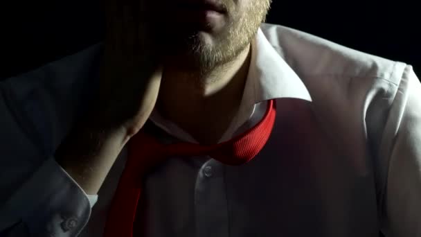 Чоловік у білій сорочці з краваткою і бородою торкається і подряпає бороду, крупним планом, чорний фон, бізнесмен — стокове відео