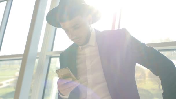 Elegante hombre caucásico en traje negro y sombrero sostiene el teléfono en su mano y leer información mientras está en el aeropuerto, primer plano, slo-mo, hombres de negocios — Vídeos de Stock