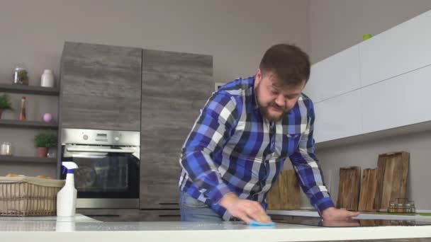 Gros homme caucasien joyeux avec une barbe faire le nettoyage dans la cuisine, laver le comptoir, intérieur moderne, ralenti — Video