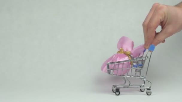 Una mano masculina está rodando un carrito de compras en el que se encuentra un huevo de Pascua, un concepto de compras para las vacaciones de Pascua, fondo blanco, espacio de copia — Vídeo de stock