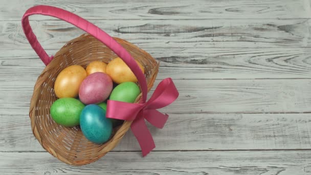 Um homem limpa uma cesta de presente com ovos de Páscoa coloridos de uma mesa de madeira, espaço de cópia, decoração — Vídeo de Stock
