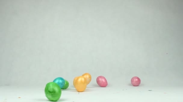 Le uova di Pasqua multicolori cadono sul tavolo, la pelle si rompe, lo sfondo bianco è il concetto della fine delle vacanze, rallentatore, spazio di copia, sfondo — Video Stock