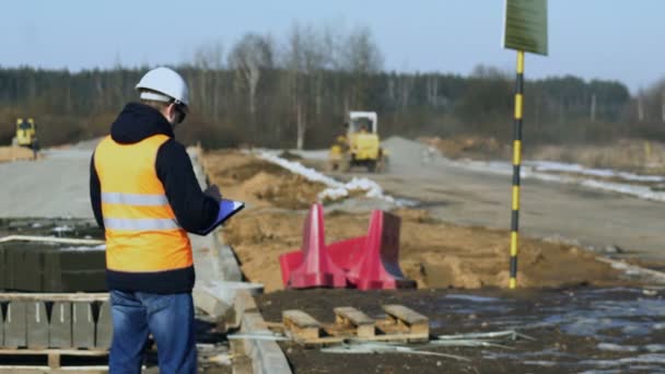 Engenheiro inspetor olha e escreve dados durante uma fase de construção de estradas antes de colocar de material de pavimento ou leito de estrada — Vídeo de Stock